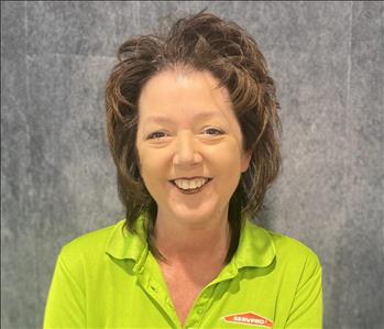 Female employee wearing lime green SERVPRO shirt standing in front of grey backdrop