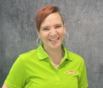 Female employee smiling energetically standing in front of grey backdrop wearing a green SERVPRO shirt