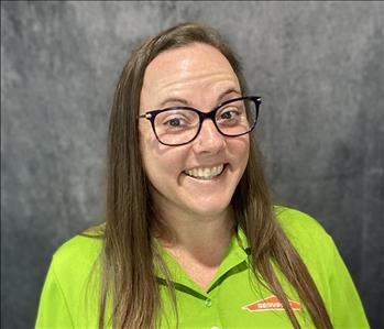 Female employee wearing a lime green SERVPRO shirt standing in front of a grey backdrop