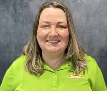 Female employee standing in front of grey backdrop with lime green SERVPRO shirt on