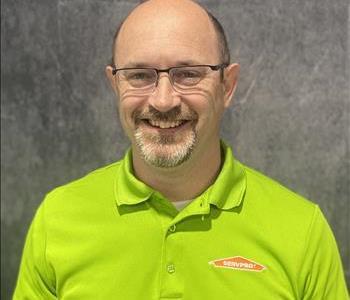 Male employee with glasses wearing lime green shirt standing in front of grey backdrop