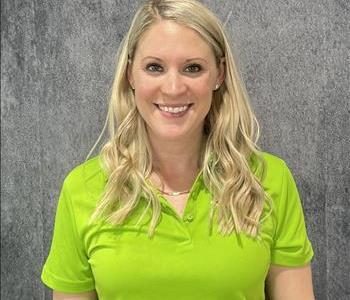 Blonde female wearing lime green SERVPRO shirt standing in front of grey backdrop